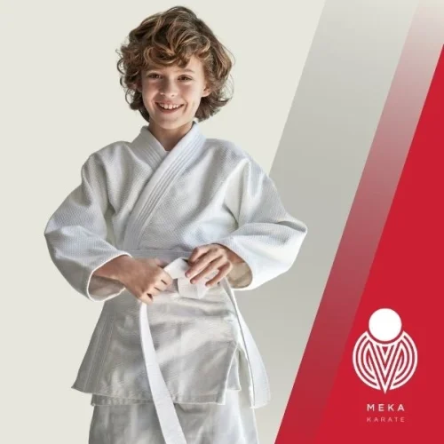 Young boy standing in a karate uniform wearing a white belt